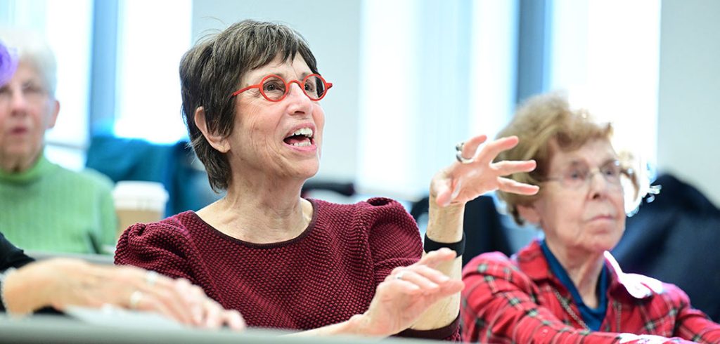 A woman with glasses raises her hand in a classroom.