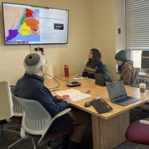 People sitting at a desk and looking at a TV screen