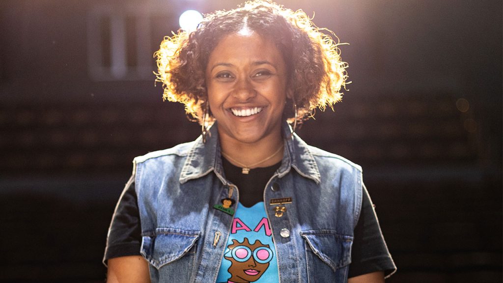 Marjuan Canady seated on a stage, smiling, with light coming from above her.