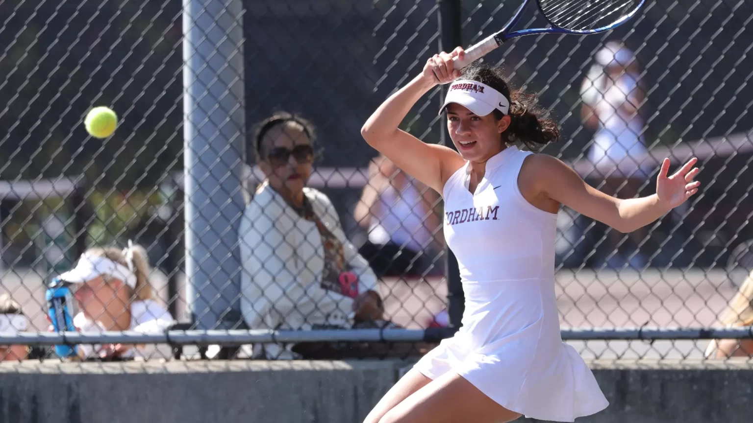 Woman in Fordham tennis uniform playing, racket in hand