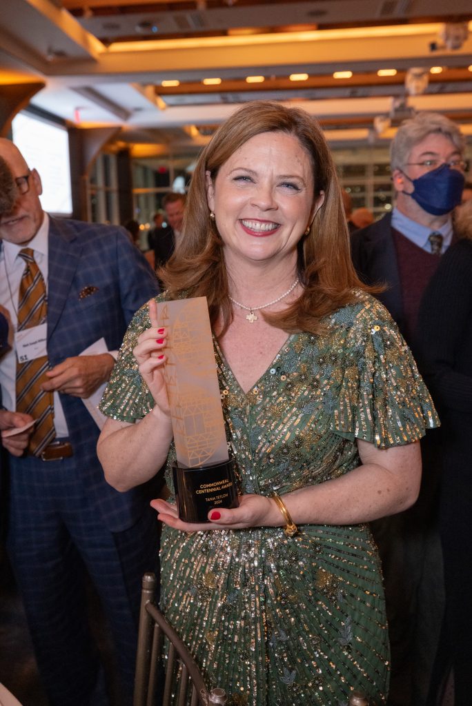 President Tania Tetlow stands holding the an award.