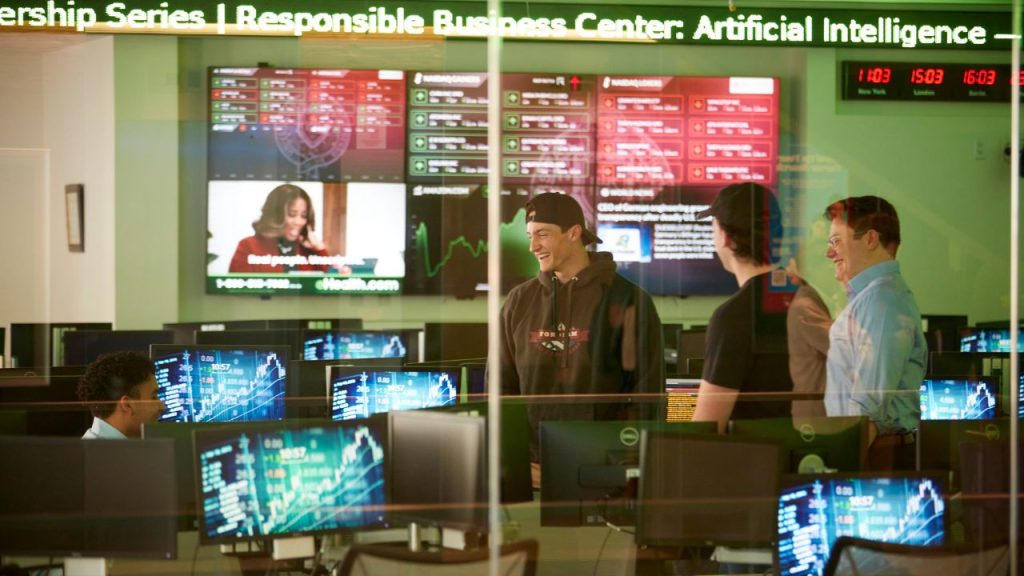 A group of four people inside a model stock exchange room at Fordham's Gabelli School of Business