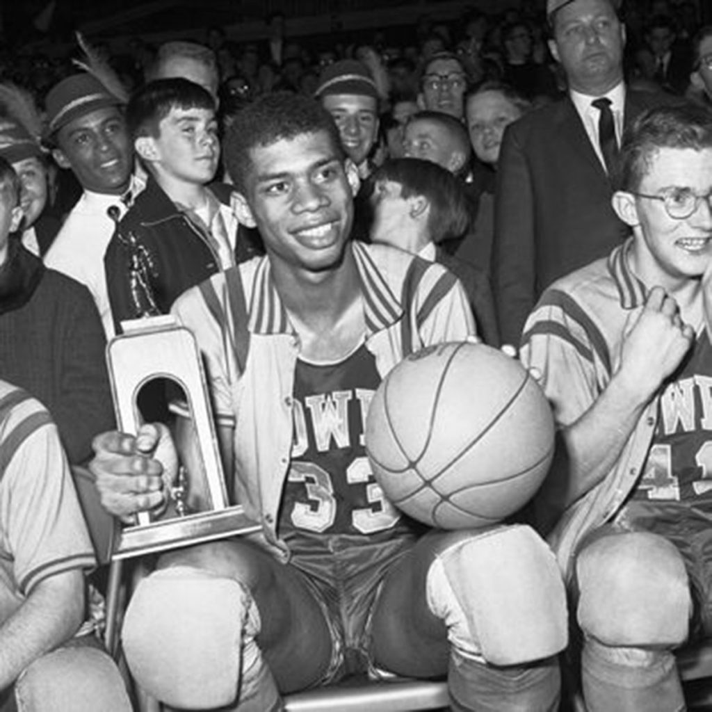 Kareem Abdul-Jabbar sits next to his Power Memorial teammates in the Rose Hill Gym and holds a basketball on one knee and a large trophy in the other