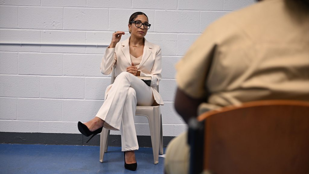 Afrika Owes, wearing a white pantsuit, speaks with women incarcerated at Rikers Island.