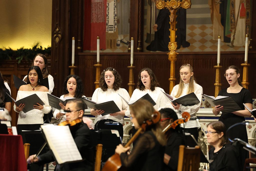 Women wearing white sing from the altar of the University Church.