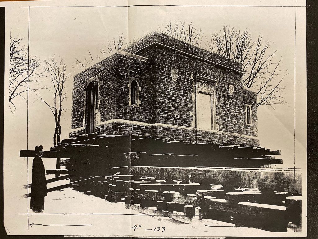 Picture of a building on logs with a man stnading alongside it. 